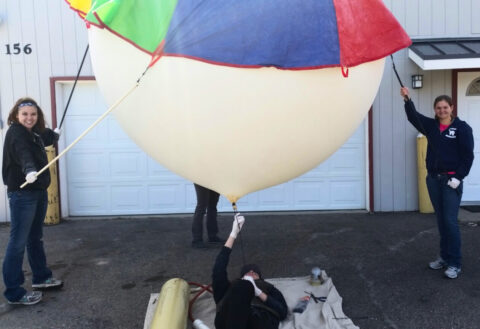 Amelia Yarborough, 18 (left), and Jamie Shultz, 17 (right), secure the balloon while Jordan Herbst, 16 (bottom), fills it with helium. Credit: Tony Phillips