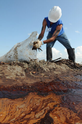 A contract worker from Health, Safety, and the Environment (HSE) loads oily waste onto a trailer on Elmer's Island, just west of Grand Isle, La., 21 May 2010 during the BP Deepwater Horizon oil spill. Credit: Patrick Kelley, U.S. Coast Guard/Marine Photobank