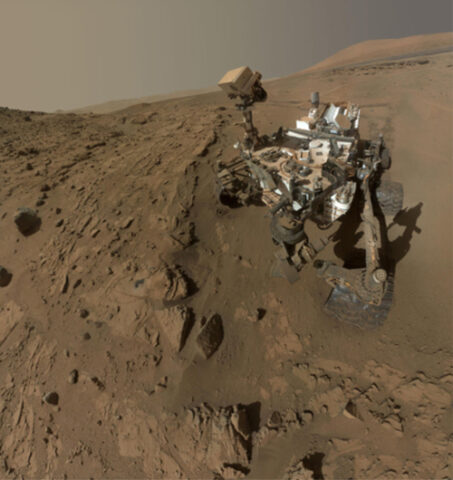 Fig. 1. Curiosity used its arm-mounted camera to take dozens of images at a sandstone drill target called Windjana that were combined into this "selfie." The view does not include the rover’s arm. Most of the frames of this mosaic view were taken during the 613th Martian day, or sol, after landing (27 April 2014). Frames showing Windjana after completion of the drilling were taken on sol 627 (12 May 2014). Aeolis Mons can be seen in the background. Credit: NASA/JPL-Caltech/MSSS.