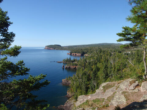 Cliffs of 1.1-billion-year-old volcanic rocks from the Midcontinent rift in Tettegouche State Park, Minnesota tower above the brilliant blue waters of Lake Superior.