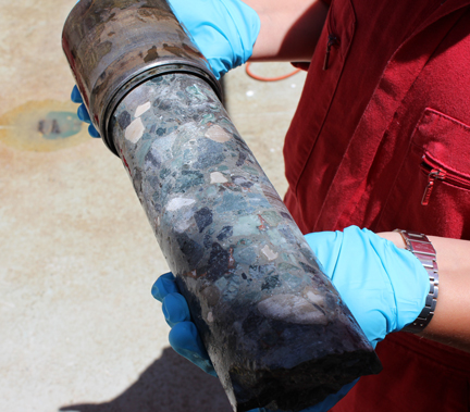 A researcher holds a core sample from the Chicxulub’s peak ring structure. The core contains broken rocks mixed up with melt fragments that were shattered and moved around within the crater during the first minutes following the impact. Credit: ARae@ECORD_IODP