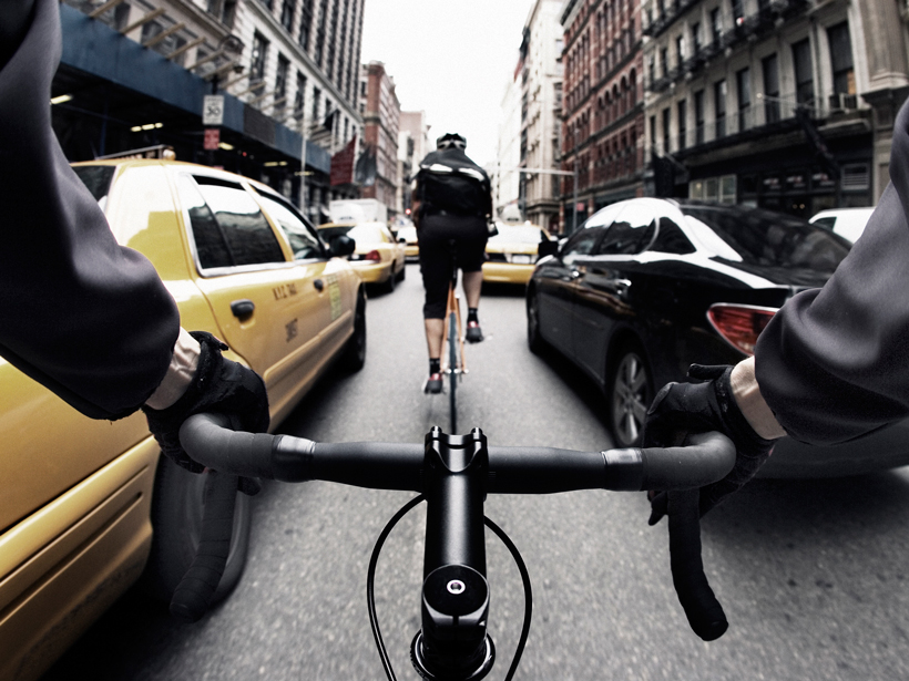 Handlebar view of a courier bicycling in New York City.