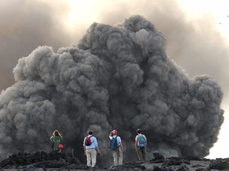 Researchers in front of a volcanic explosion at Yasur volcano in Vanuatu, which is ejecting volcanic ballistic projectiles and a small ash plume. Photo: AGU's Eos/Marco Albano