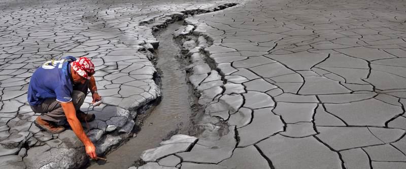 A scientist examines one of the streams flushing water and mud spewed by the geysering Lusi vent site.