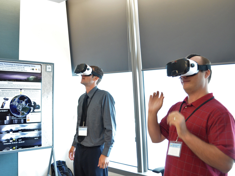 Two men wearing virtual reality headgear stand beside their poster exhibit at NOAA's second Emerging Technologies Workshop.