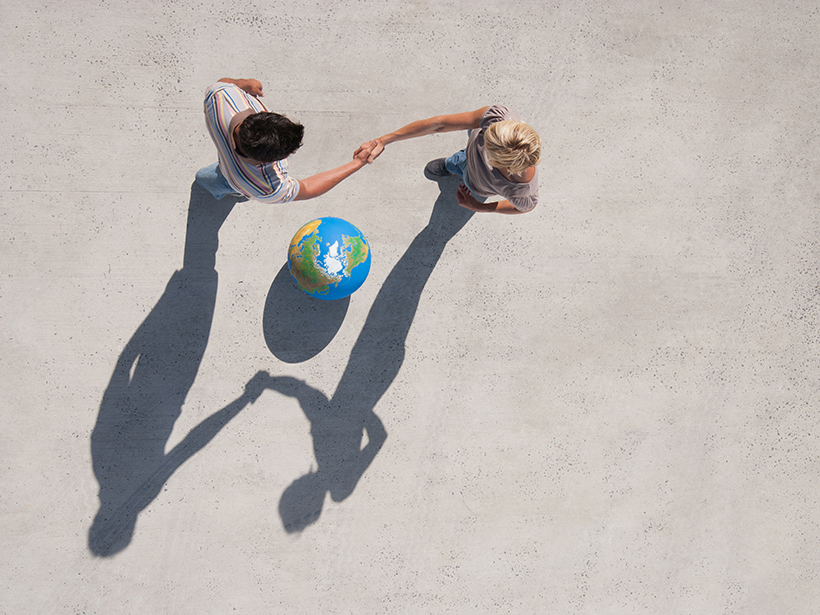 Aerial view of two people shaking hands beside a globe and their shadows.