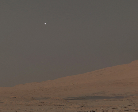Phobos sets over Mt. Sharp, Mars, in a mosaic of three images captured by the Curiosity rover in 2014.