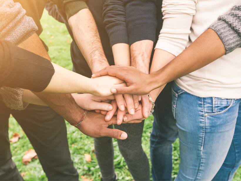 Photo of hands—men's and women's, different skin tones—clasped in a huddle.