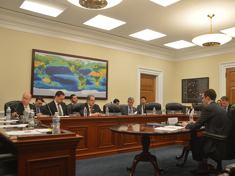 A panel of men question another man at a table