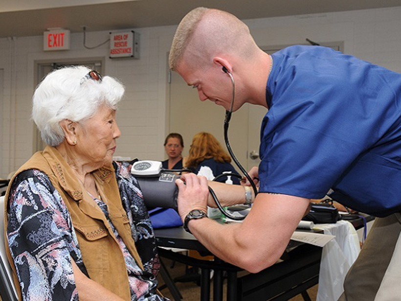 A young man takes the blood pressure of an older woman.