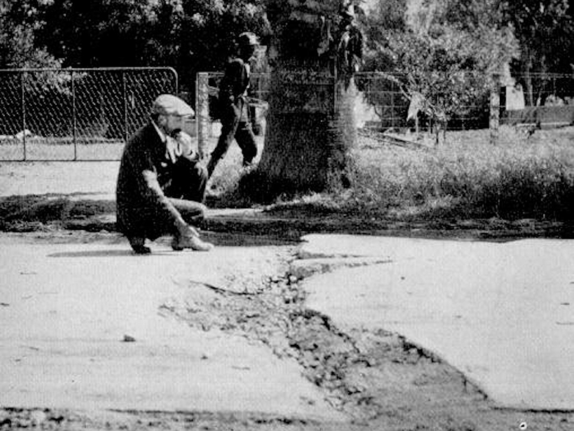 A man kneels next to a road cracked by the 1928 San Jacinto earthquake.
