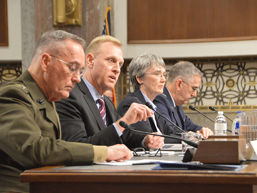 Three white men and a white woman testify in front of a small bank of microphones.