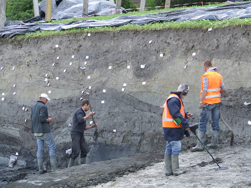 Workers excavate an earthy cliff beneath grassy turf.