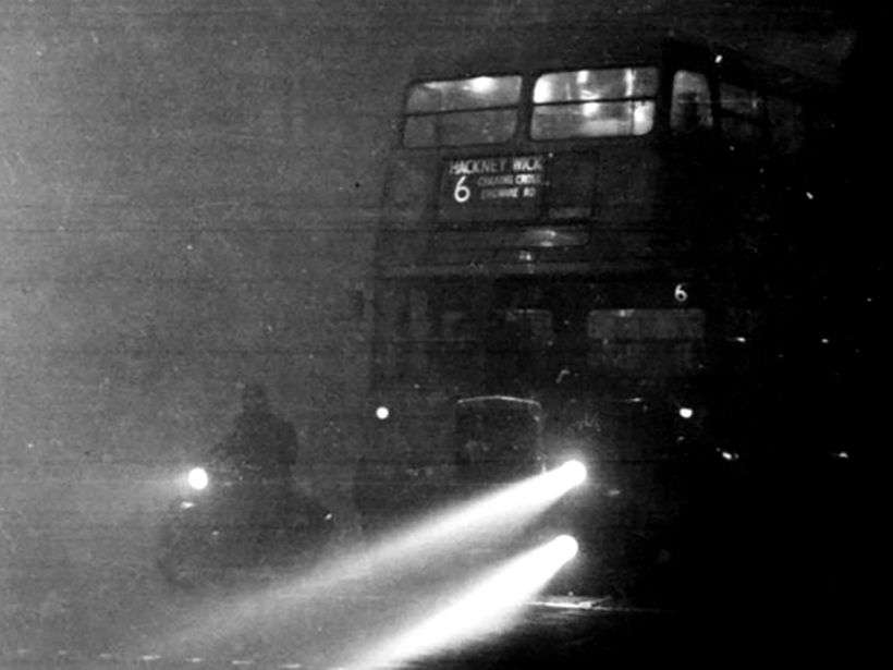 Black-and-white photo of a motorcycle and double-decker bus in thick fog