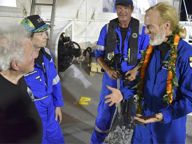 Three people listen while a guy in a lei talks animatedly on the deck of a ship