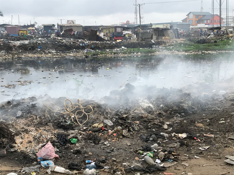 Steam rises from garbage and a polluted river.