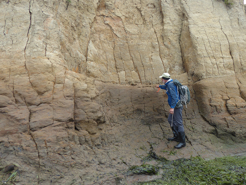 Geologist points at a rock feature in a cliff.