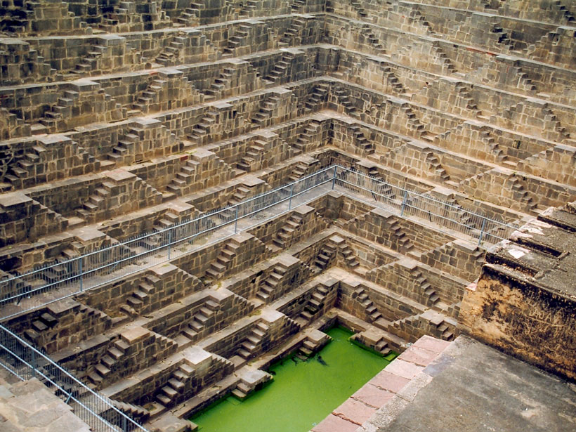Photo of a deep stepwell in India, with a green pool at the bottom