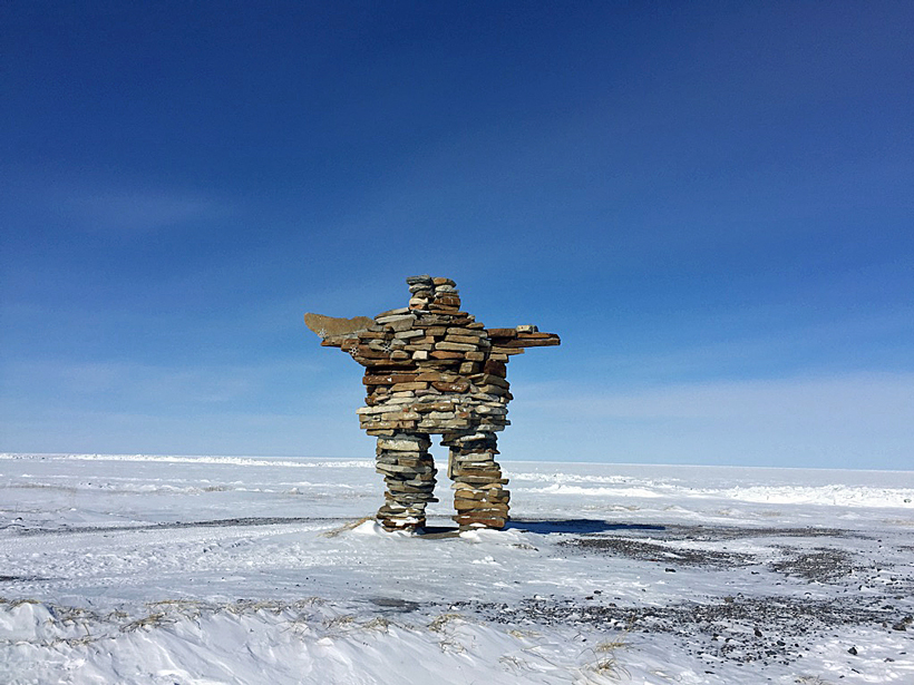 An Inuit stone landmark called an inukshuk overlooks the sea ice at Kuujjuarapik, Nunavik, Canada.