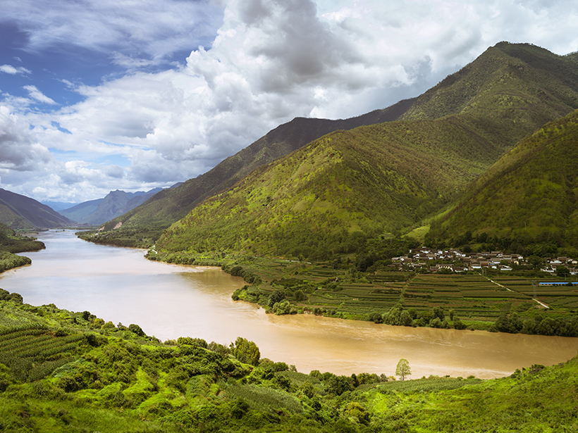Photo of the Yangtze River flowing through a valley lined with greenery and agricultural terraces in China