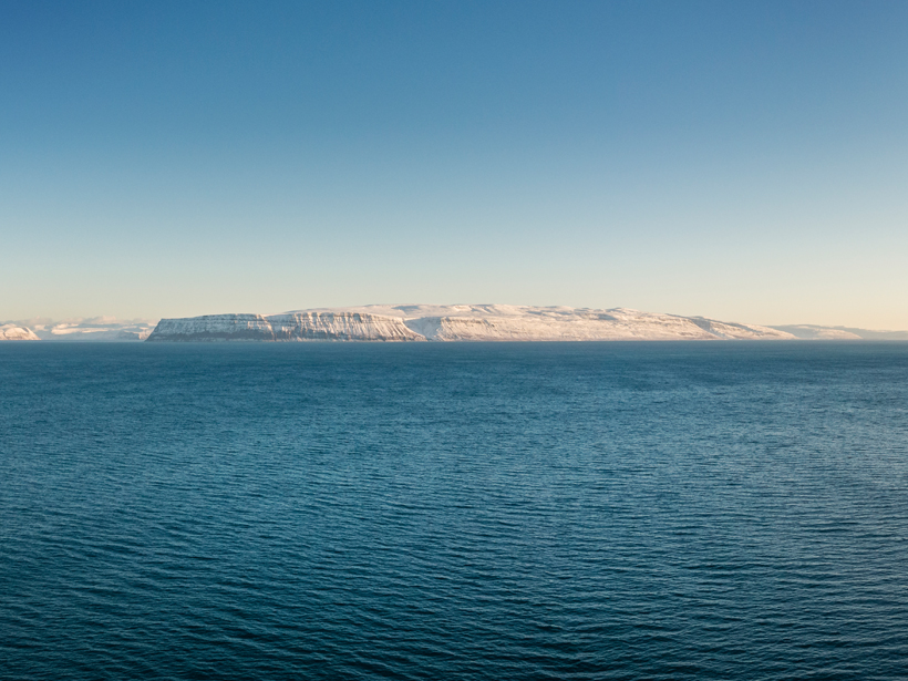 A stretch of the North Atlantic Ocean with the snow-covered shoreline of western Iceland in the background