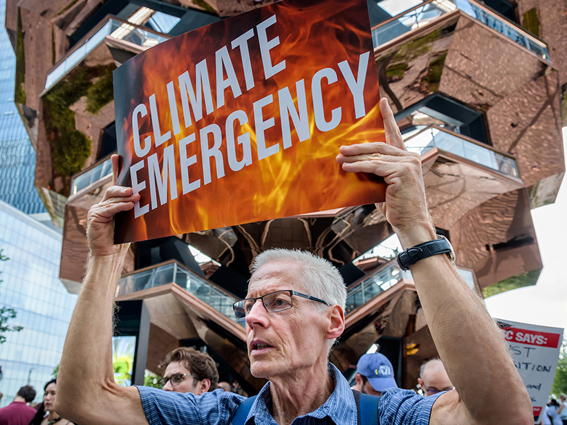 White man holds sign outside CNN climate town hall reading “Climate Emergency”