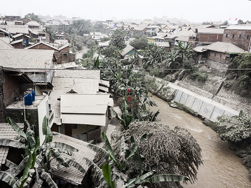 Photo of an ash-covered, densely populated tropical neighborhood and canal