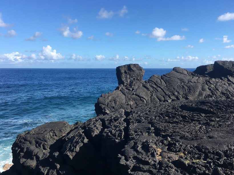 A landscape of dark volcanic rocks forefronts a beautiful blue ocean.