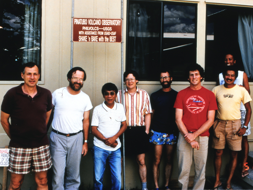 Eight men stand in front of a sign reading “Pinatubo Volcano Observatory.”