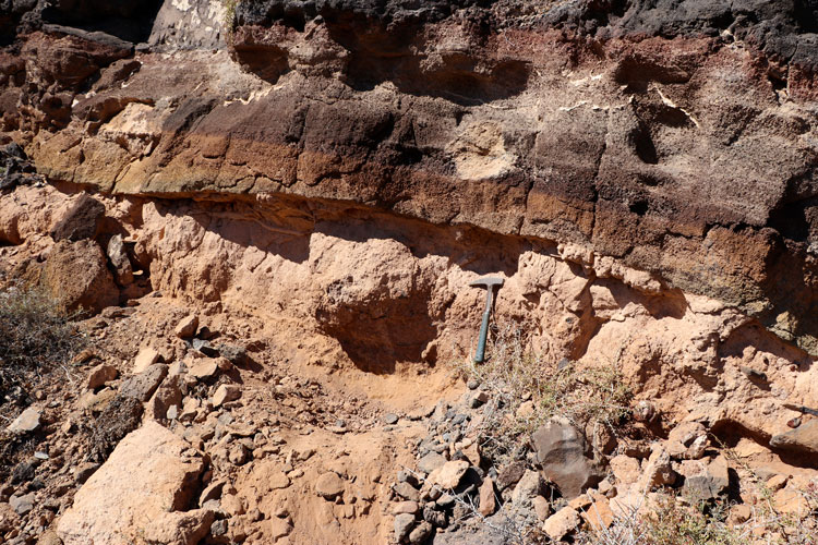 Rock hammer provides scale for layers of reddish and brownish rock layers
