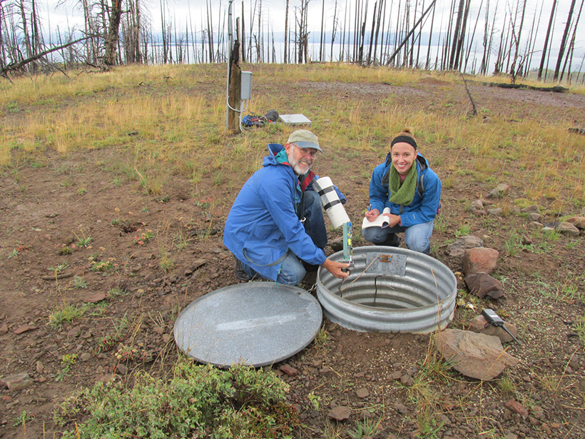 Two smiling scientists kneel to check equipment in an underground seismometer.