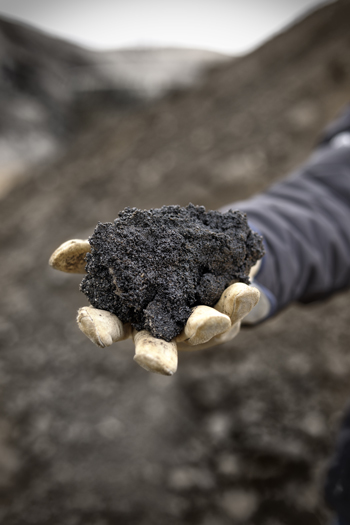 A gloved hand holds a chunk of black oil-soaked sand