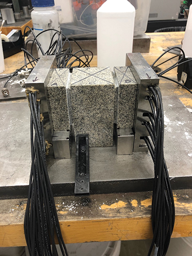 A rock sample is sandwiched between sensor-equipped steel plates. A rock sample is sandwiched between sensor-equipped steel plates.