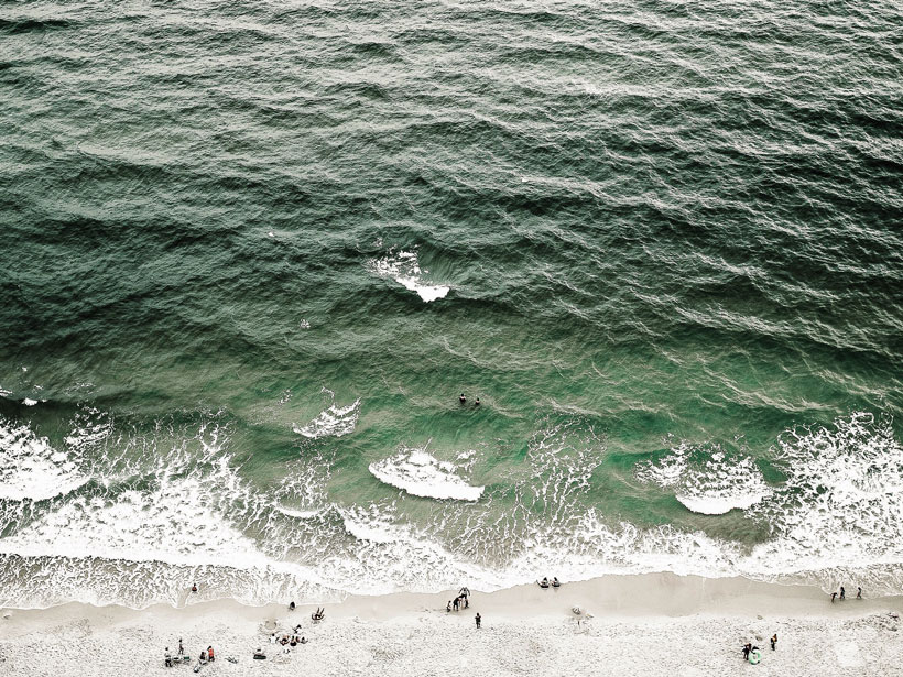 Aerial photo of waves lapping at a beach with people near the shore