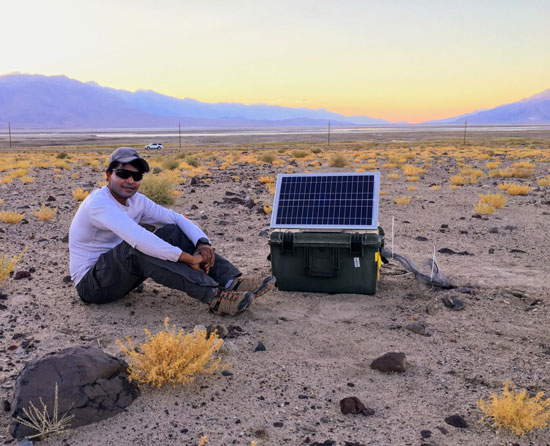 Photo of a man sitting in a rocky desert with a small solar-powered seismic station Photo of a man sitting in a rocky desert with a small solar-powered seismic station