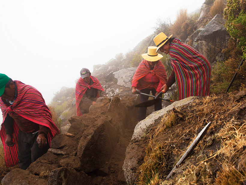 An image of villagers from Huamantanga constructing a shallow stone canal to divert water down a hillside