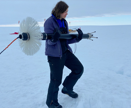 A woman carries a large device across the ice.