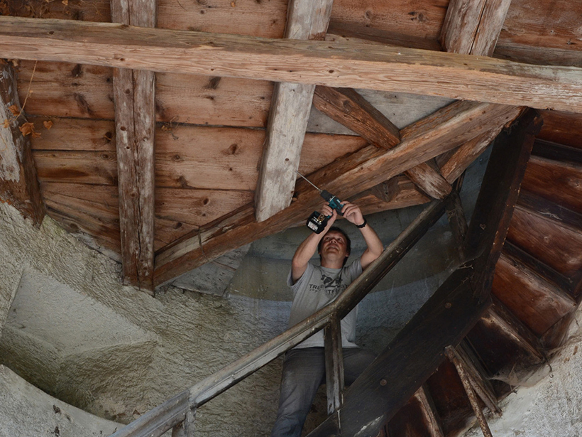 A man uses a tool to extract a tiny sample of a construction timber in a wooden roof.