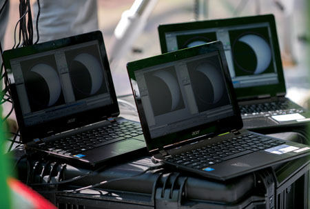 Three laptops display images of a solar eclipse