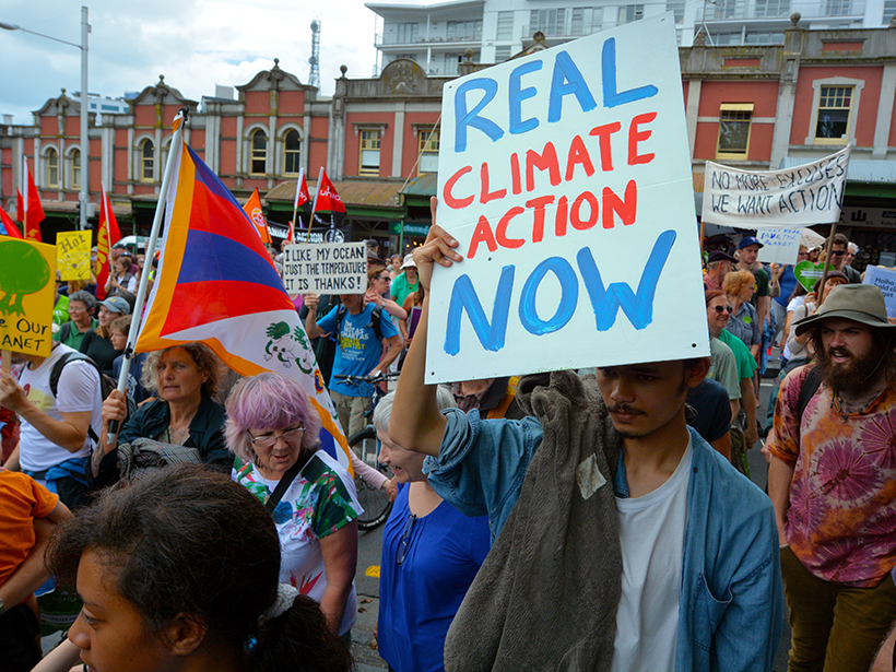People march in a climate protest, with signs reading “Real Climate Action Now”