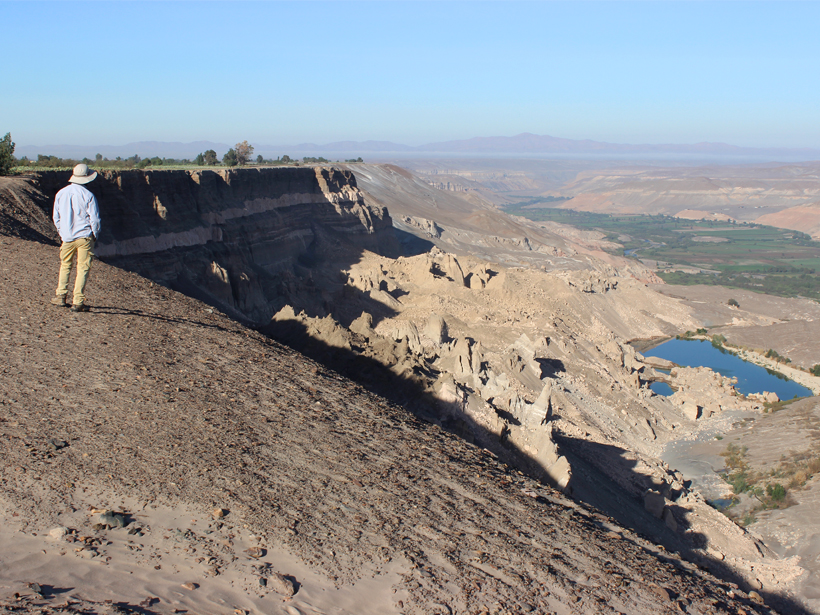 Man overlooks a fertile farming valley abutted by dry cliff walls.