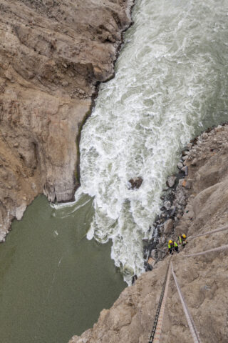 Photo of people scaling a vertical rock face above a surging river Photo of people scaling a vertical rock face above a surging river