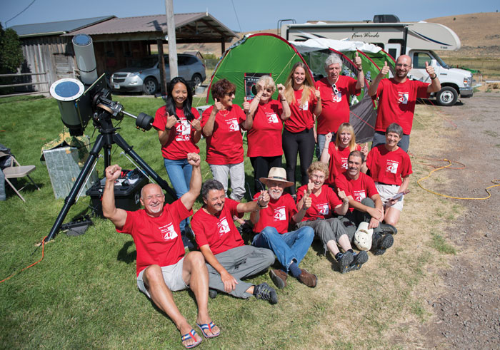 Team of scientists give a thumbs-up in front of tents and telescopes on a rural ranch