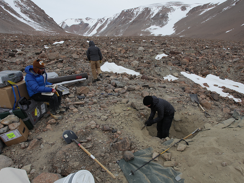 Three scientists, one digging a hole, sample soil from a dry valley in Antarctica.