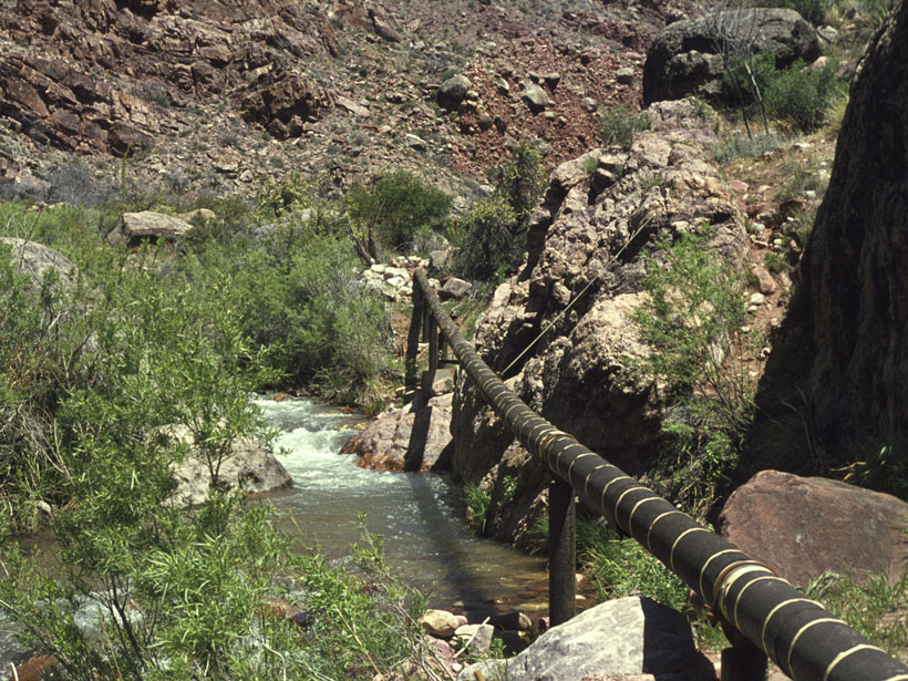 A pipeline stretches across a flowing river in a small canyon.