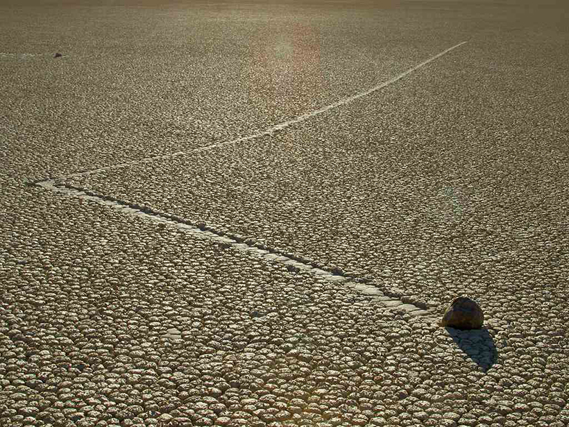 Rock leaves a trail on a cracked, dry lake bed.