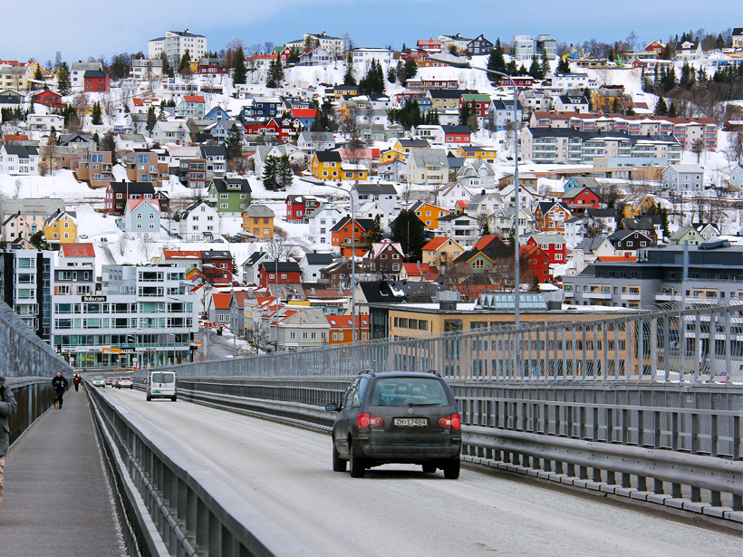 A clean two-lane road leads into a sunny winter day in Tromsø, Norway.