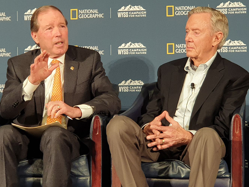 Sen. Tom Udall and former secretary of the interior Bruce Babbitt sit on a dais with National Geographic logos everywhere