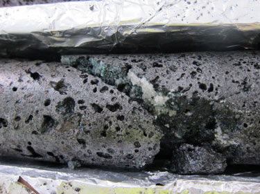 A black, porous basalt core with white carbonate crystals