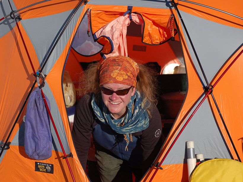 Glaciologist Erin Pettit, in a bandana and sunglasses, smiles from the door of a tent in Antarctica.